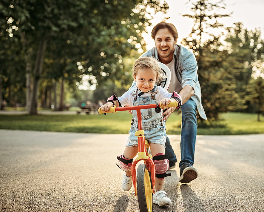 Adulto enseñandole a montar en bicicleta a niña.